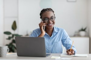 Office Trainee. Black woman talking on cellphone and taking notes at workplace